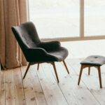 A contemporary armchair and footstool in a minimalistic room with sunlight streaming through large windows.